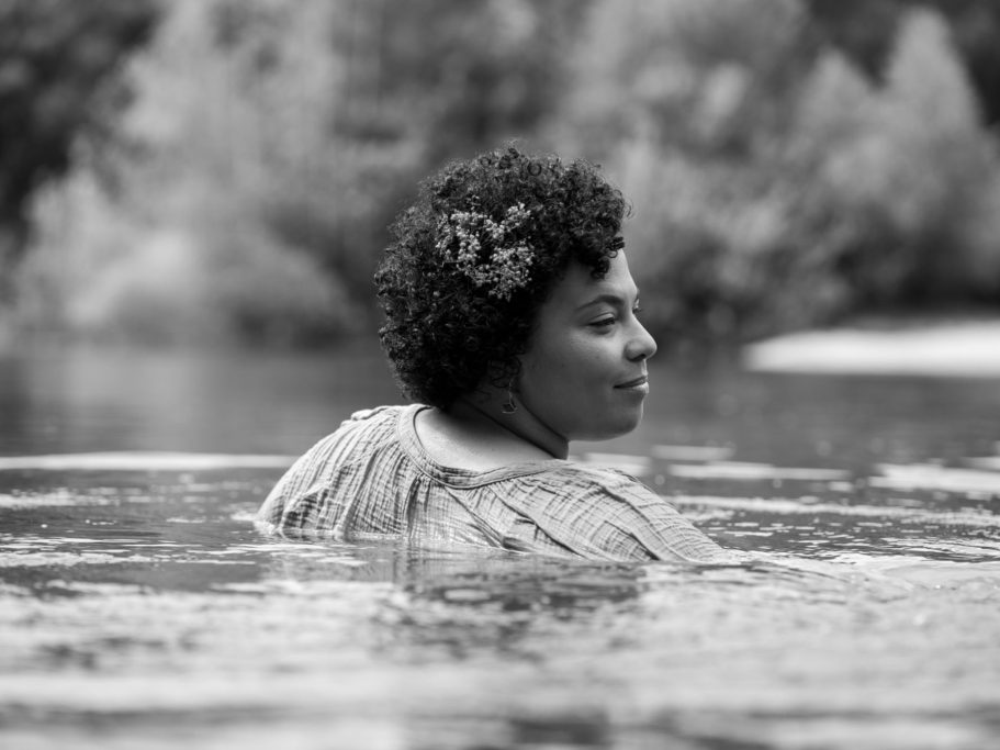 Erblüht – Frauenporträts für Women of Color Frauenporträt einer Woman of Color mit Afro-Haaren im Wasser, umgeben von natürlicher Landschaft
