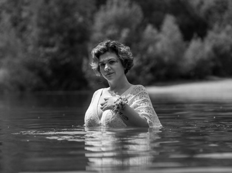 Erblüht Body and Soul Stories Frau mit Blumenkranz in einem Gewässer, umgeben von Bäumen im Hintergrund.Empowerment und Portraitfotografie in Schleswig Holstein