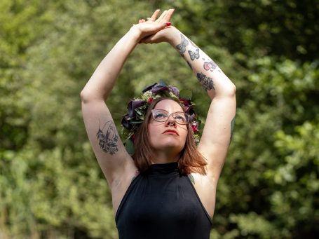 Selbstliebe Shooting Erblüht Frau mit Blumenkranz, die die Arme in die Höhe hebt, vor grünem Hintergrund.