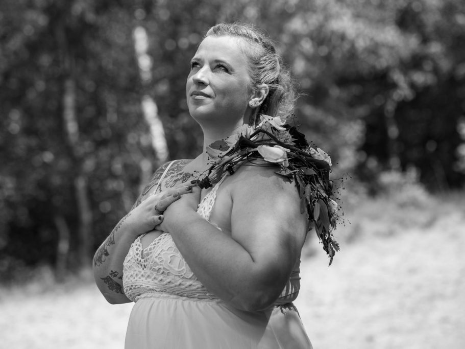 Erblüht – Selbstliebe in Bildern Frauenportrait- Frau in einem hellen Kleid steht lächelnd mit gefalteten Händen in der Natur.