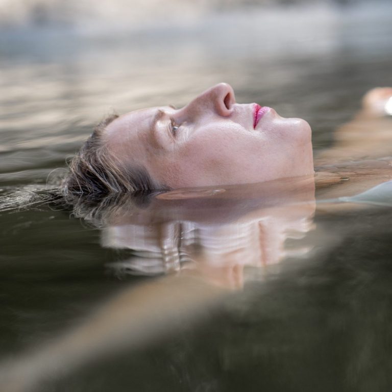 Empowerment Fotoshooting im Wasser | Body & Soul Stories Frau treibt entspannt im Wasser, Gesicht zum Himmel, Empowerment Fotografie für Frauen in Schleswig-Holstein